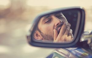 Side mirror view sleepy tired yawning man driving car | Does Driver Fatigue Make You More Likely to be in an Accident