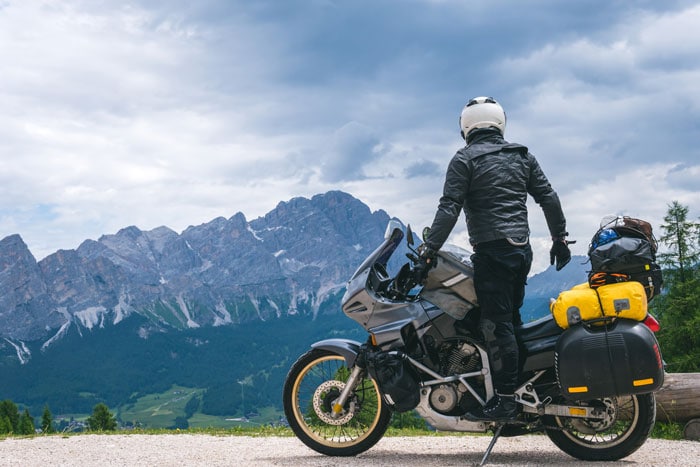 person standing on a parked motorcycle looking at mountains