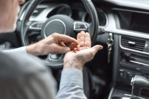 man putting pills in his hand behind the wheel | Drugged Driving Accidents