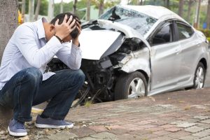 distraught man next to totaled car | Most Common Accidents To Avoid This Holiday Season